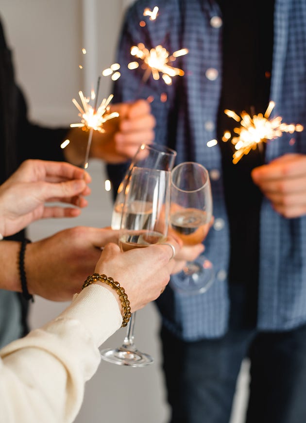 Three people each hold a lit sparkler and glass of champagne,